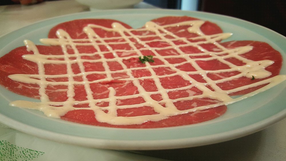 Beef carpaccio with white sauce drizzled in a crosshatch pattern on a light blue plate